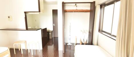 A hotel room with a bed, a desk, a mirror, a window with curtains, and a bathroom visible through an open door.