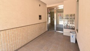 A hallway with a tiled floor, a trash bin, and a row of mailboxes. - Enzo Shin-Osaka C (Osaka)