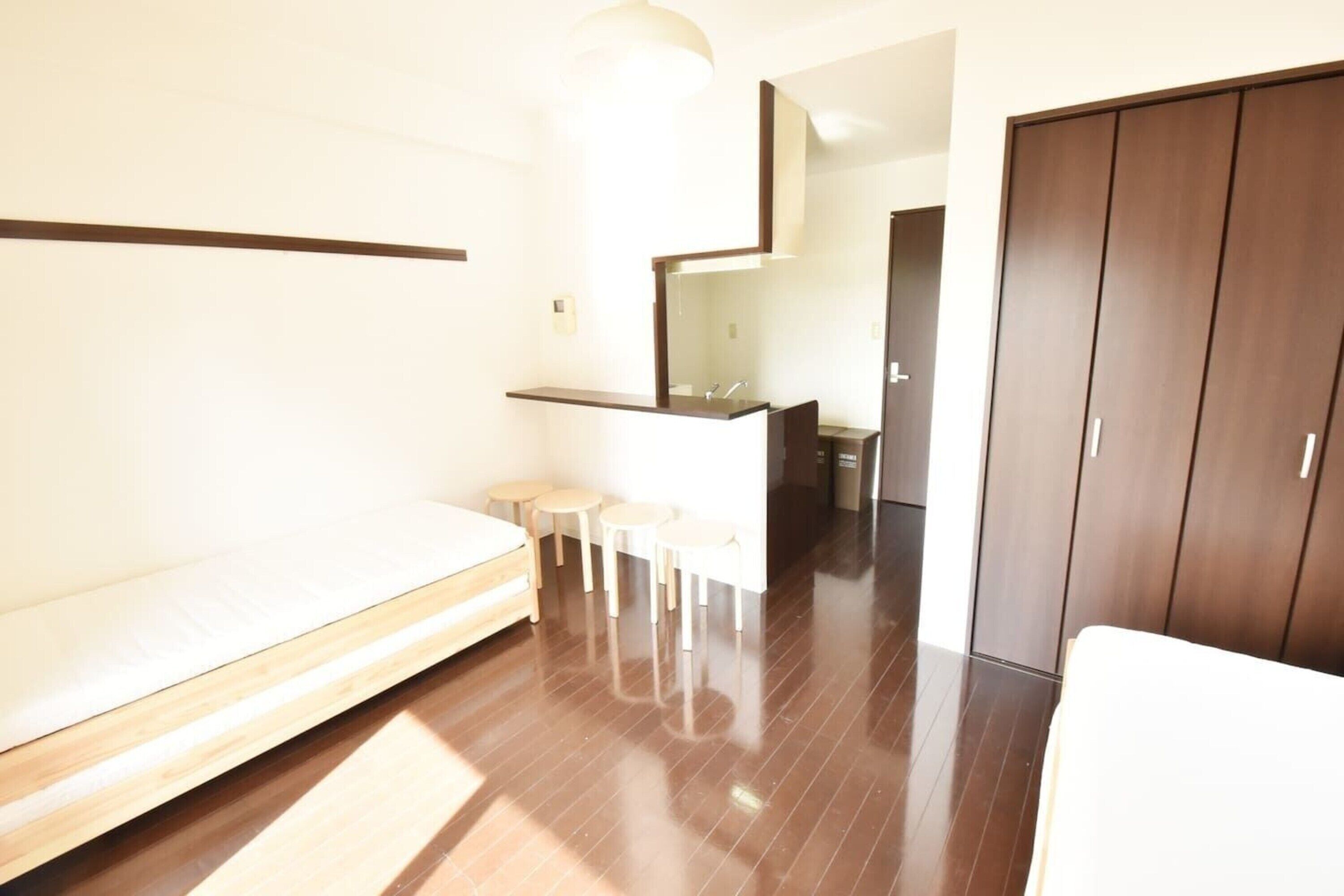 A modern bedroom with a wooden floor, a bed, a small seating area, a mirror, and a wardrobe.