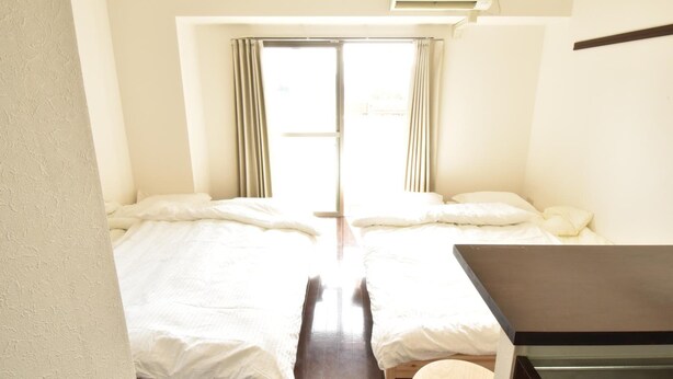 A room with two beds, a small table, and a window with curtains. - Enzo Shin-Osaka C (Osaka)