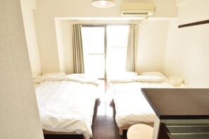 A room with two beds, a small table, and a window with curtains. - Enzo Shin-Osaka C (Osaka)