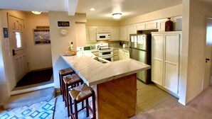 A kitchen with white cabinets, a large island with stools, stainless steel appliances, and a clock on the wall. - Mountain Getaway (Mammoth Lakes)