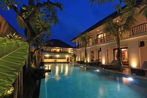A pool area with lounge chairs, a building with balconies, and tropical plants. - Elite Cassia (Tibubeneng)