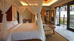 A spacious bedroom with a large bed, a sitting area with a chair, and a balcony with a view. - Elite Cassia (Tibubeneng)