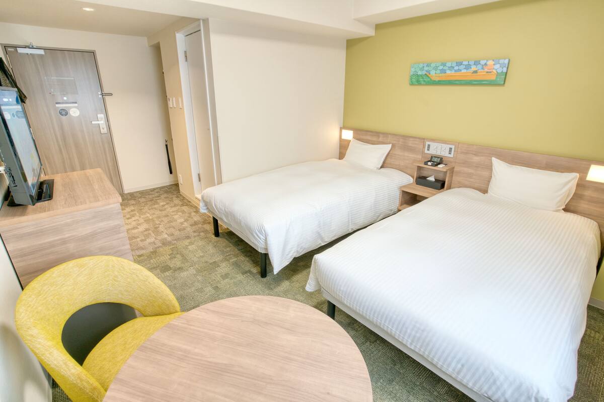 Ein Hotelzimmer mit zwei Betten, einem Schreibtisch, einem Stuhl und einem kleinen Tisch.