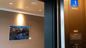 Innenansicht eines Aufzugs mit Bedienfeld von Fujitec, einem an der Wand hängenden Bild mit Flusslandschaft und einer Decke mit eingelassener Beleuchtung.