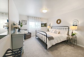 A bedroom with a bed, bedside lamps, a dresser, a chair, and a mirror.