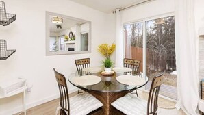 A dining area with a glass table surrounded by chairs, a large mirror on the wall, and a view of a backyard through a sliding glass door. - Midnight Sun Retreat - Close to Trails, Shopping (Anchorage)