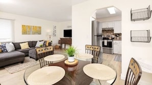 A modern living room with a dark wood dining table, a gray sofa, and a kitchen in the background. - Midnight Sun Retreat - Close to Trails, Shopping (Anchorage)