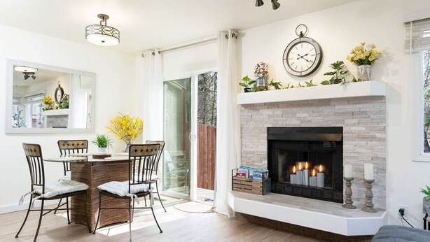 A dining area with wicker chairs and a round table, a fireplace with lit candles, and a clock on the wall. - Midnight Sun Retreat - Close to Trails, Shopping (Anchorage)