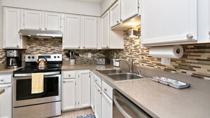 A modern kitchen with white cabinets, a stainless steel stove, and a tiled backsplash. - Midnight Sun Retreat - Close to Trails, Shopping (Anchorage)