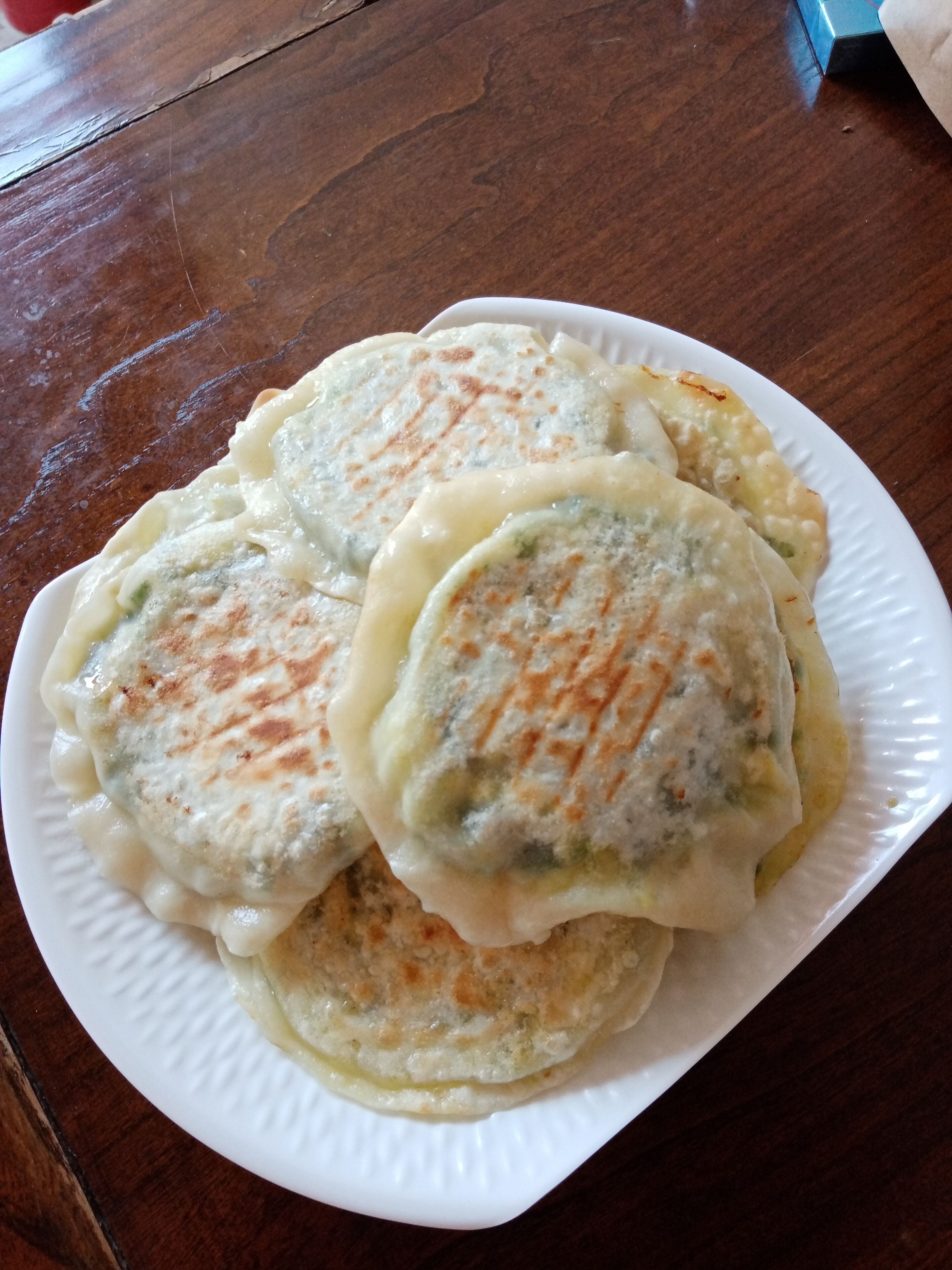En tallerken med flade brød, synlige grønne krydderurter og en gylden skorpe, serveret på en hvid papirtallerken.