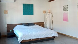 A bedroom with a wooden ceiling, a bed with white bedding, a small bedside table, and a wall-mounted air conditioner.