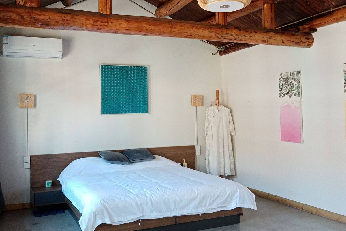 Un dormitorio con techo de madera, una cama con ropa blanca, una mesita de noche pequeña y un aire acondicionado instalado en la pared.