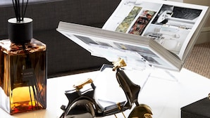 A modern living room with a white coffee table, a black and gold scooter model, a scented candle, and a magazine. - Watford WD17 - Stunning 2 Bed Flat near Watford Junction (Watford)