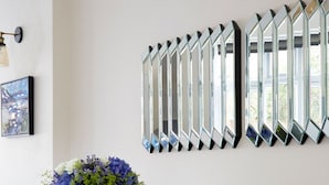 A dining area with a white table, two grey chairs, a vase of flowers, and a wall-mounted mirror display. - Watford WD17 - Stunning 2 Bed Flat near Watford Junction (Watford)