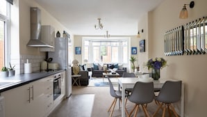 A modern kitchen with a central island, a dining area with a table and chairs, and a living room with a sofa and a coffee table. - Watford WD17 - Stunning 2 Bed Flat near Watford Junction (Watford)