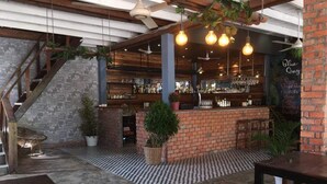 Zona bar interna con bancone in mattoni, lampadine pendenti e piante in vaso.