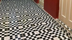 Un corridoio con pavimento a scacchi bianco e nero, pareti rosse e uno specchio che riflette una zona cucina.