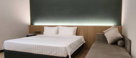A modern hotel room with a large bed, a bedside table, a sofa, and a wall-mounted TV.