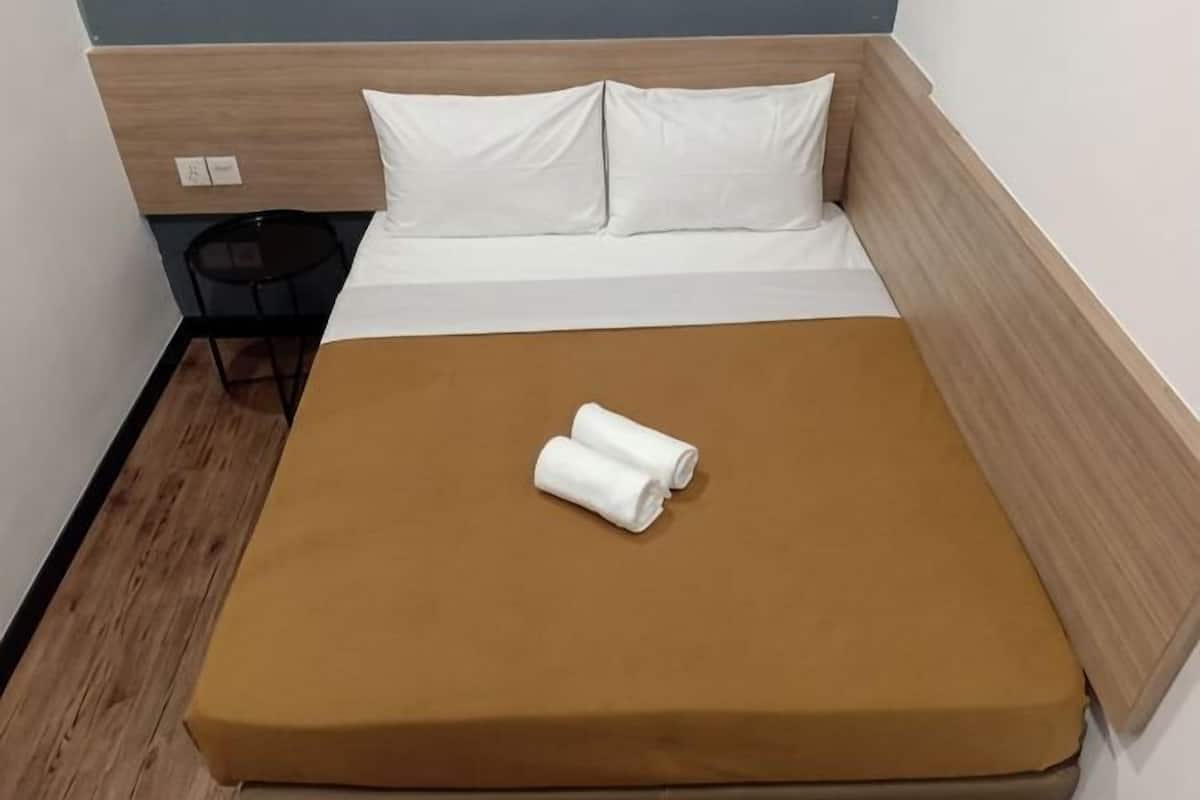 A single bed with a brown mattress, white pillows, and a rolled white towel.