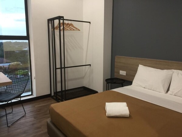 A hotel room with a bed, a chair, a small table, and a hanging clothes rack.