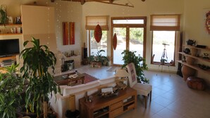 Un salon spacieux avec un haut plafond, des poutres en bois, une cheminée, un téléviseur et diverses plantes.