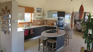 Une cuisine moderne dotée d’un îlot central, de poutres en bois au plafond et d’un coin repas avec des tabourets de bar.