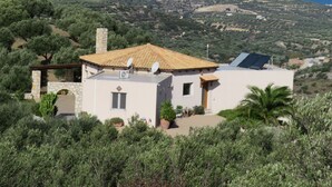 Une maison avec un toit en tuiles, des antennes paraboliques et des panneaux solaires, entourée de verdure et offrant une vue sur un paysage vallonné.