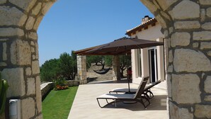 Une terrasse extérieure avec des murs en pierre, un sol carrelé et un espace salon couvert comprenant des chaises et une table.