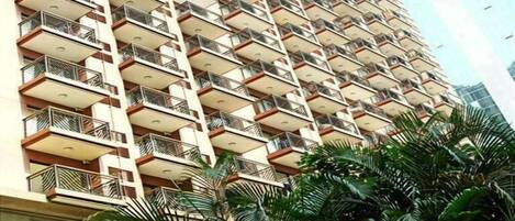 A high-rise building with multiple balconies, surrounded by lush green trees.