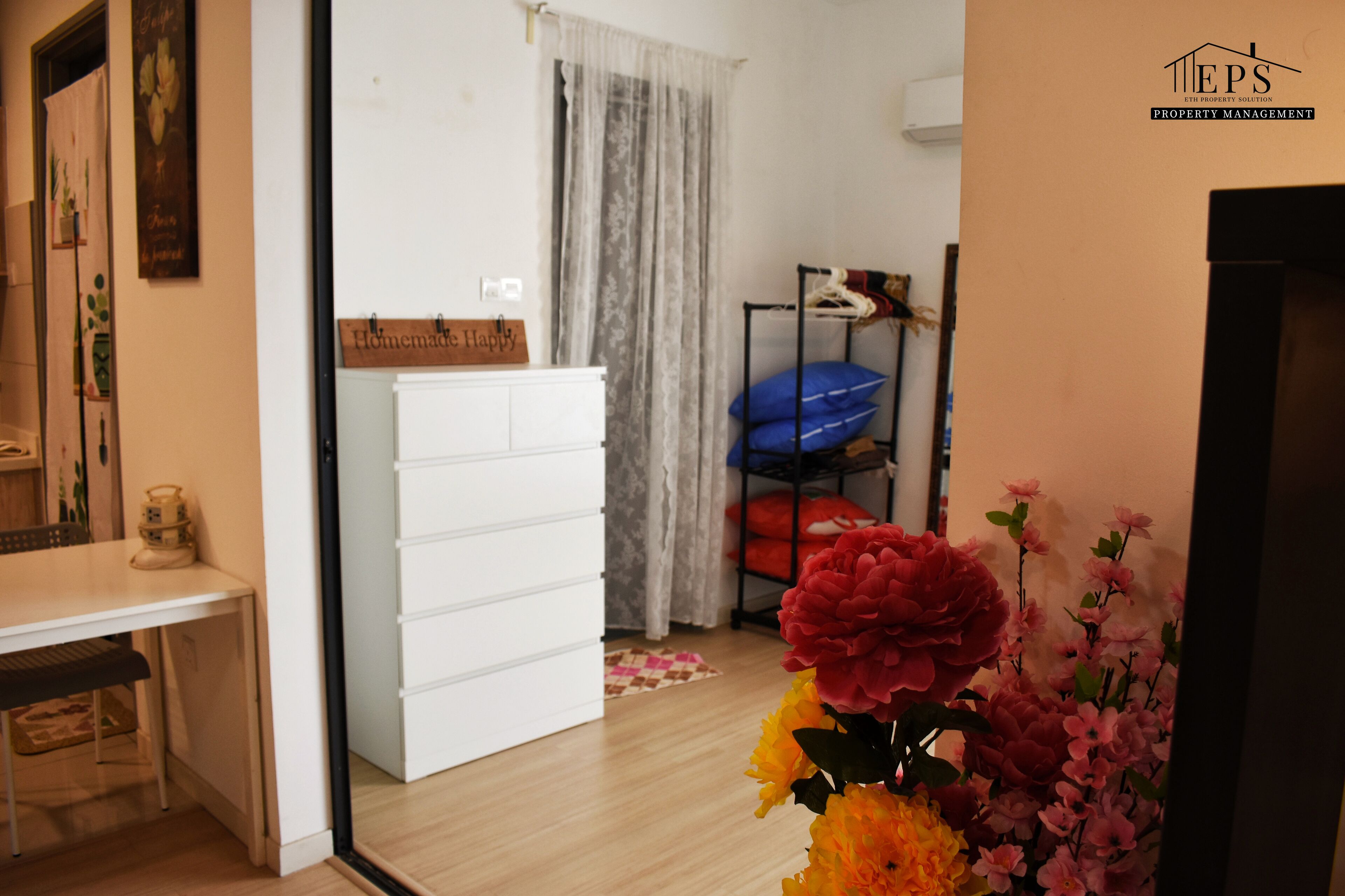 A room with a white dresser, a bed with a blue mattress, and a floral arrangement.