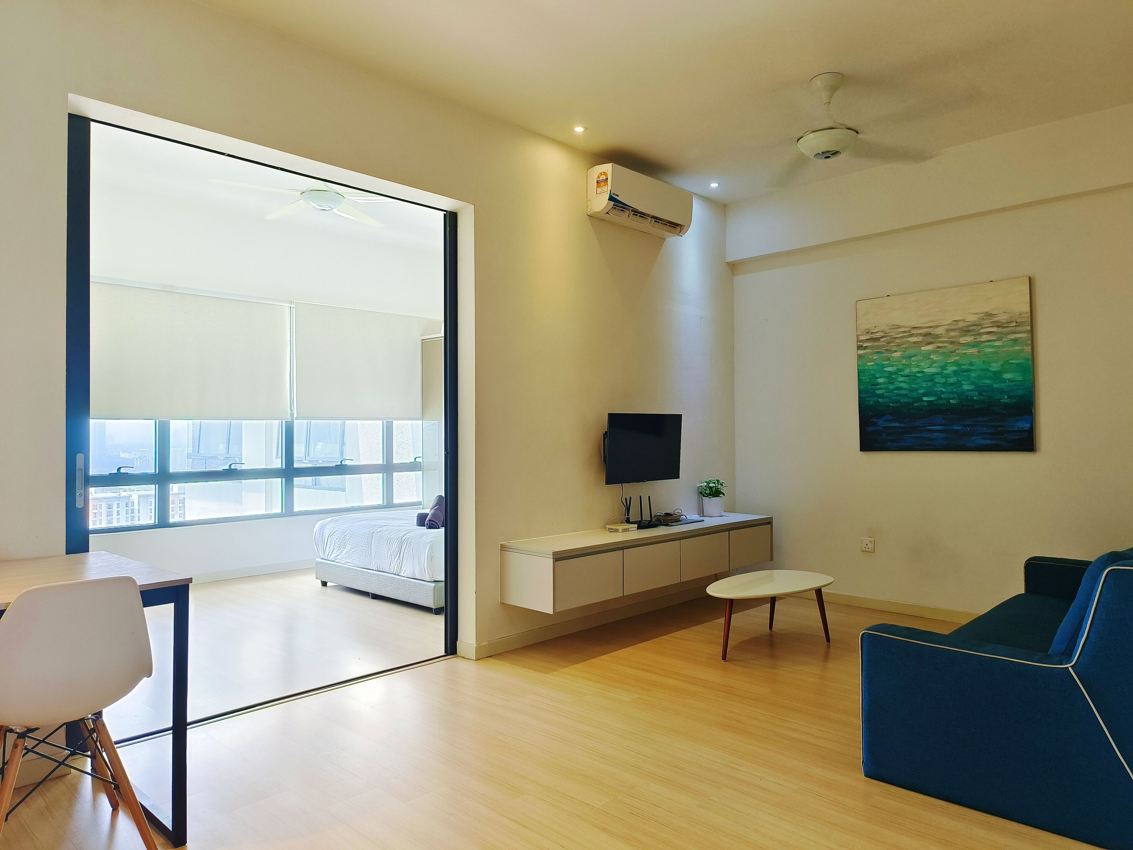 A modern living room with a sofa, a dining table with chairs, a TV, and a painting on the wall.