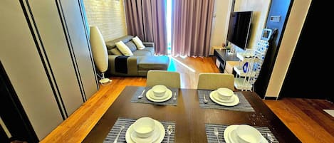 A modern dining area with a wooden table set for four, a sofa, and a television in the background.