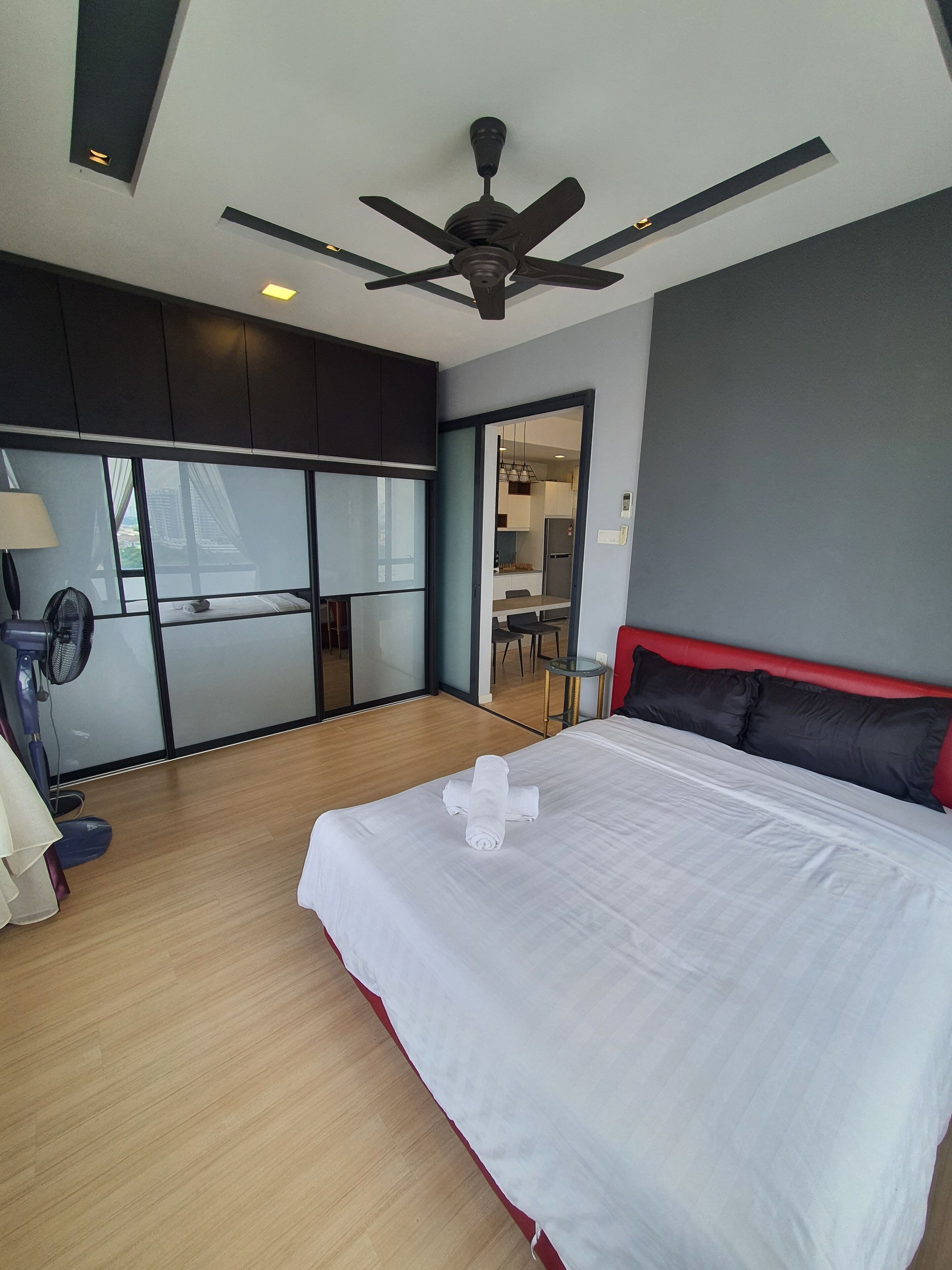 A hotel room with a bed, a ceiling fan, a desk, and a view of the outside.