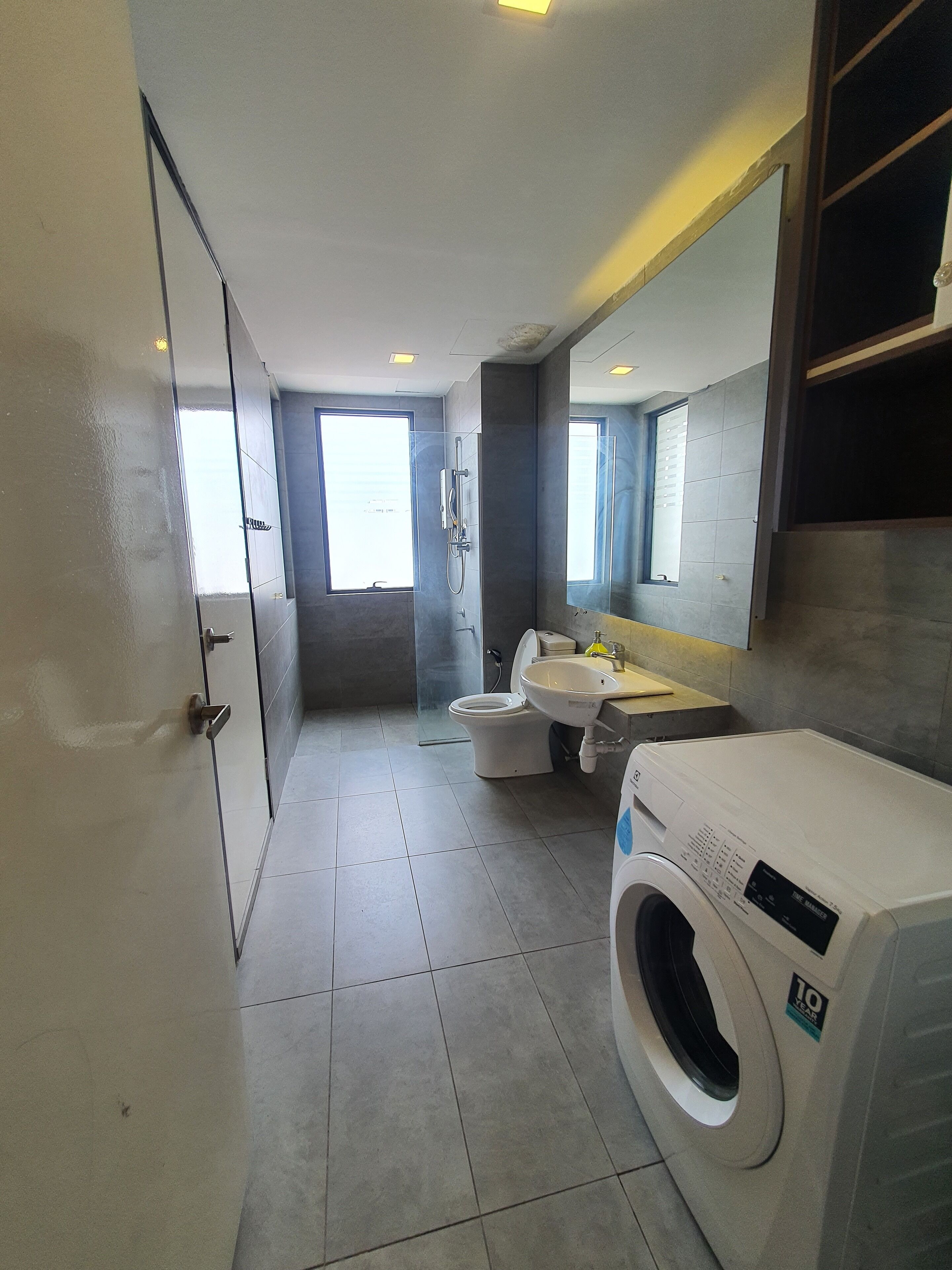 A modern bathroom with a toilet, sink, and washing machine, featuring large windows and a tiled floor.