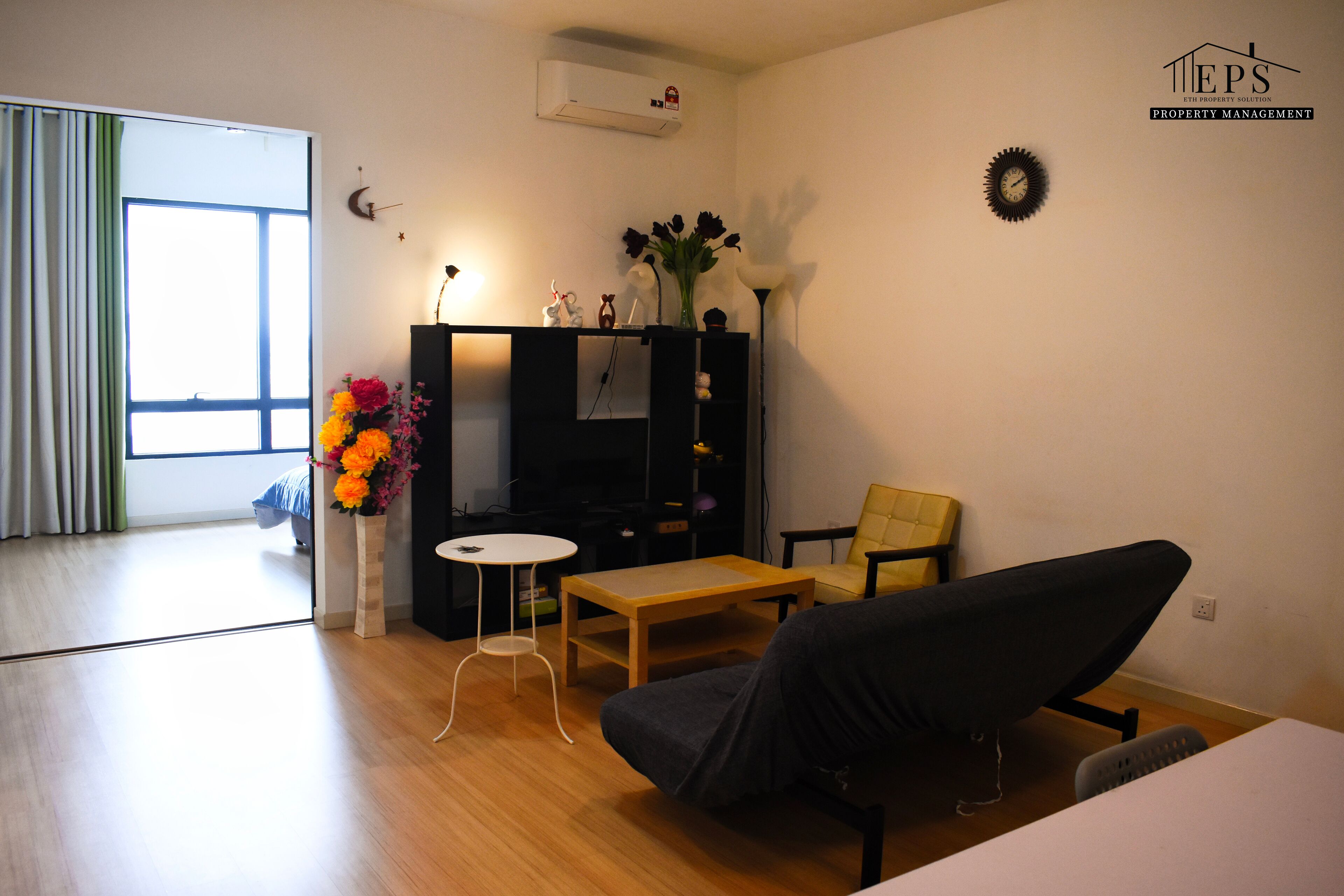 Ein modernes Wohnzimmer mit einer Couch, einem kleinen Tisch, einem Fernseher und einer dekorativen Vase mit Blumen.