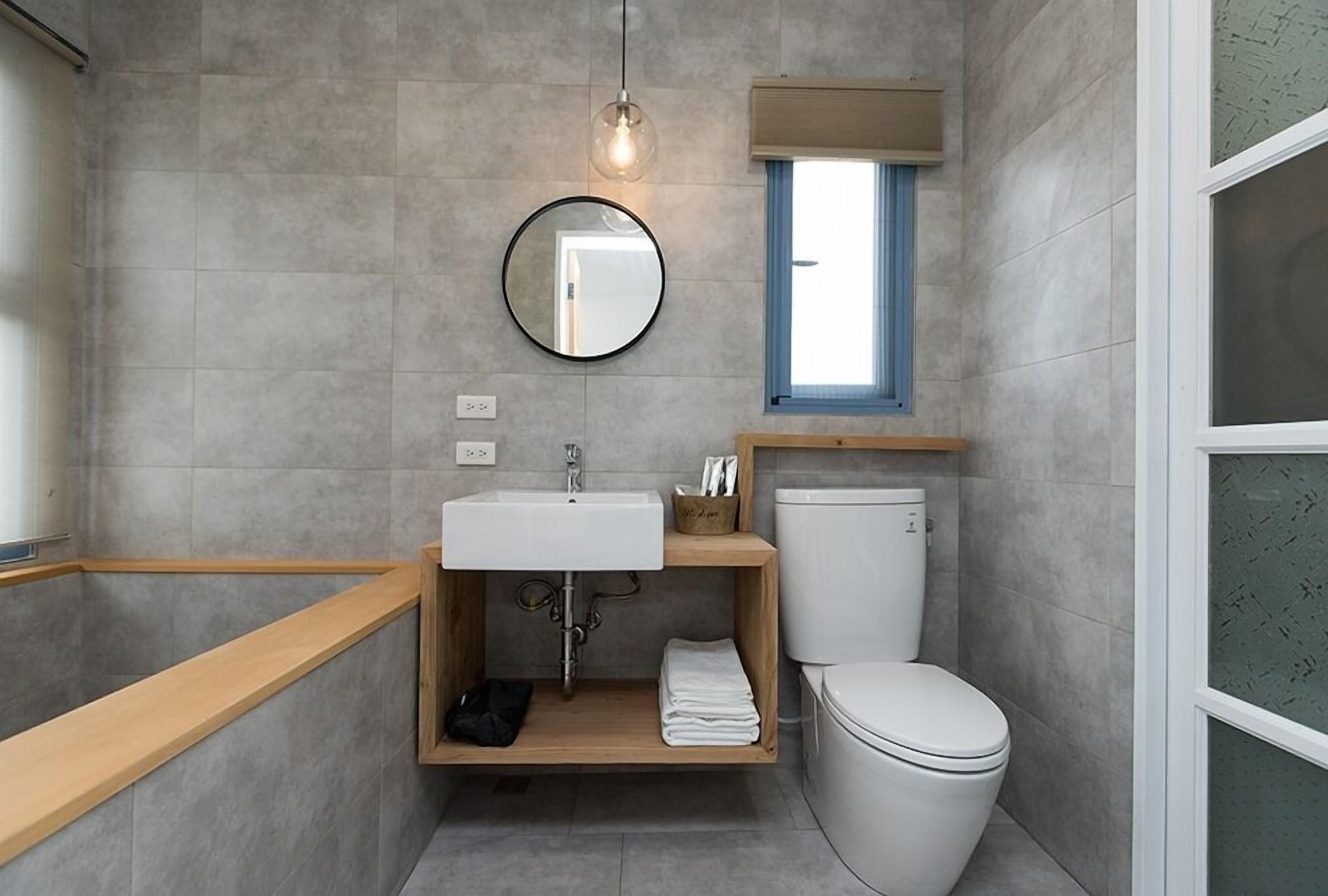 A modern bathroom with a wooden vanity, a round mirror, a toilet, and a bathtub.