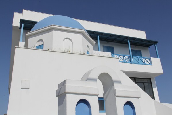 Ein weißes Gebäude mit blauen Akzenten, darunter ein Balkon mit blauen Geländern und eine kuppelförmige Struktur.