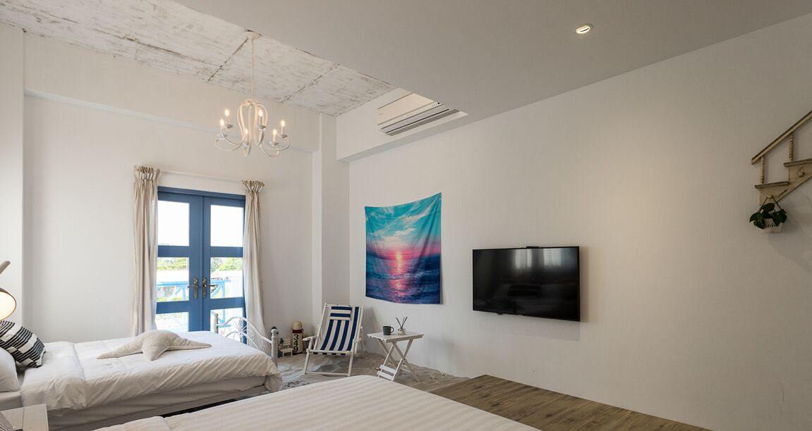 Une chambre avec deux lits, une télévision, un tableau et une fenêtre avec des rideaux.