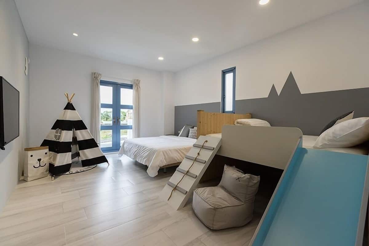 Une chambre moderne comprenant un lit, un espace nuit, une fenêtre et un téléviseur fixé au mur.