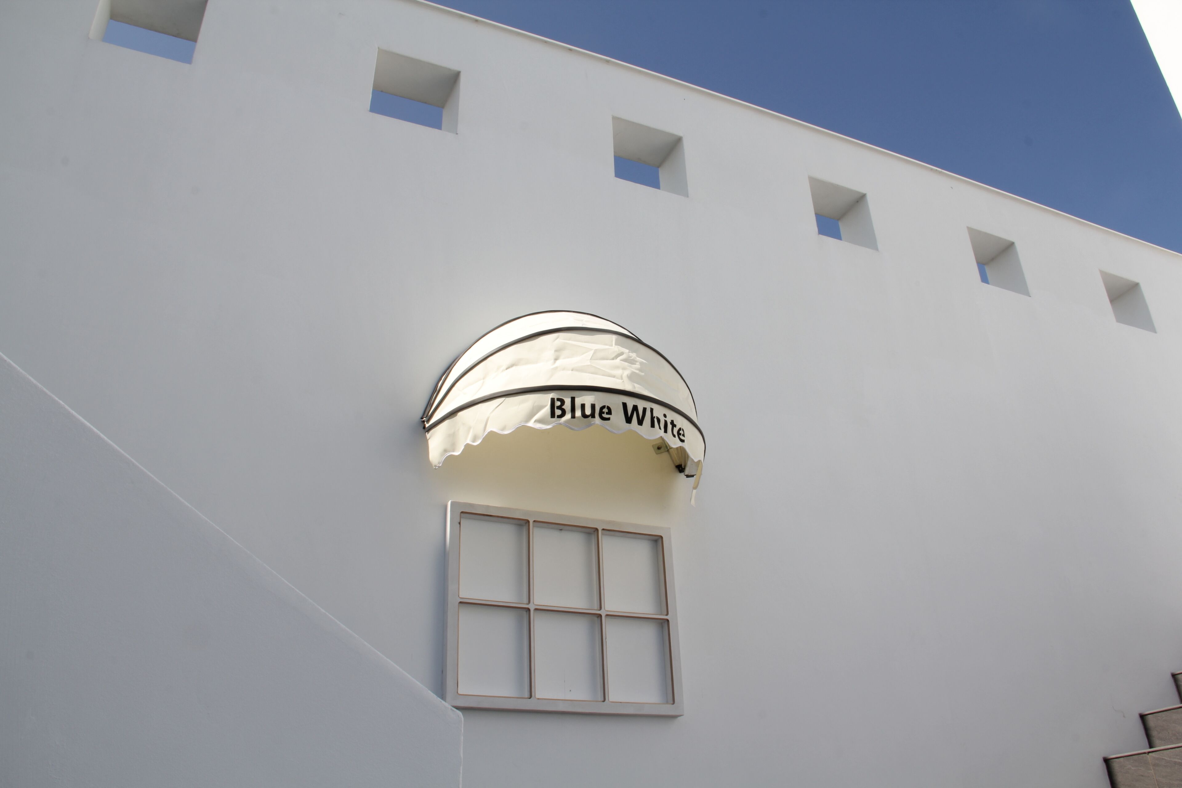 Un edificio con facciata bianca, una finestra con vetri a griglia e un cartello con su scritto 'Blue White'.