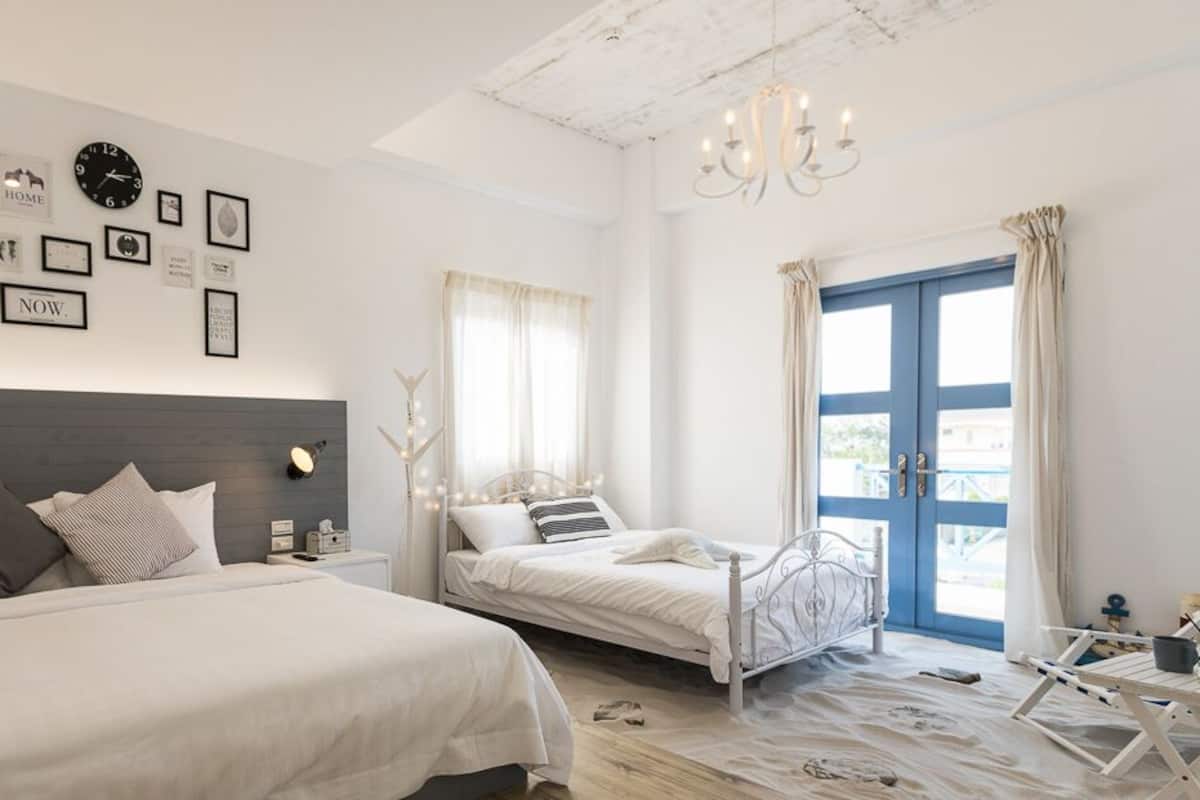 Une chambre avec deux lits, un lustre, une grande fenêtre avec des rideaux et des œuvres d’art murales.