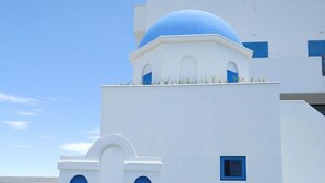 Um edifício branco com detalhes em azul e uma cúpula, apresentando janelas em arco e uma pequena varanda.