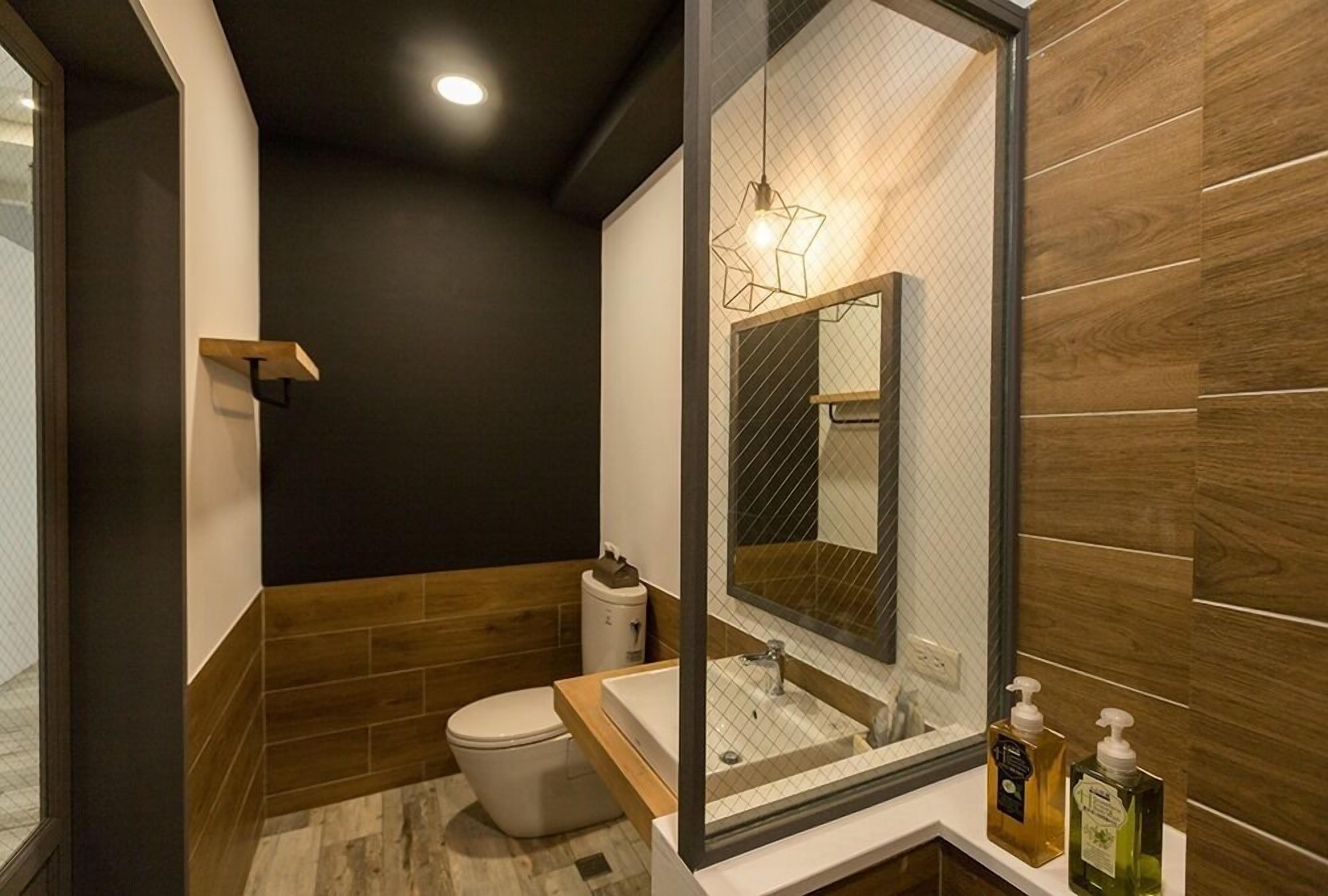 A modern bathroom with a wooden floor, a white toilet, a sink with a mirror, and a shower area.
