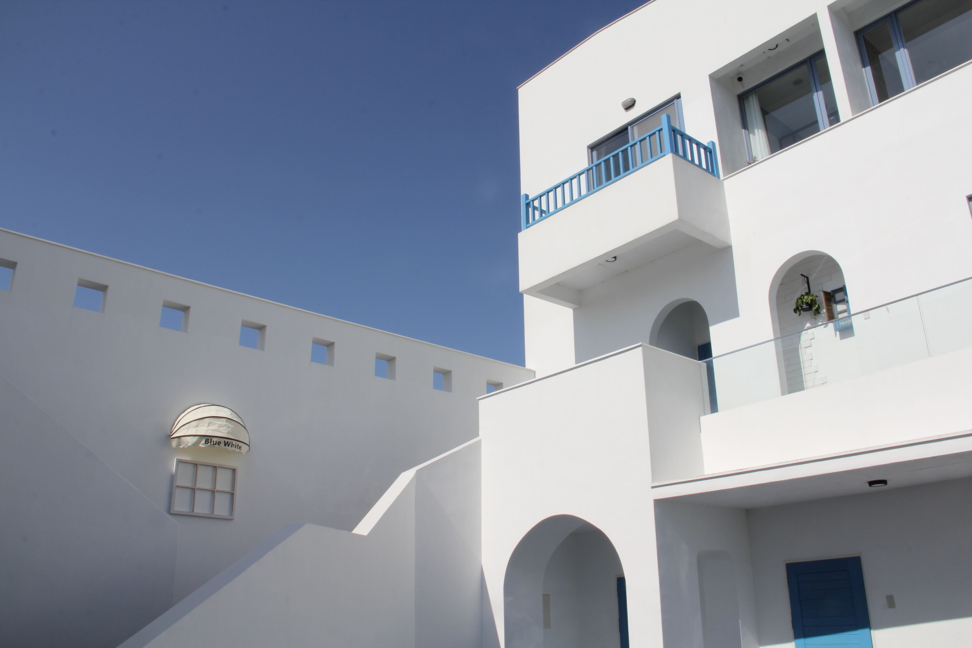A white building with a blue balcony and arched windows.