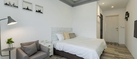 Un dormitorio moderno con una cama, un sofá gris, una mesita de noche, una lámpara y arte mural que representa Lisboa, Bangkok y Marsella.