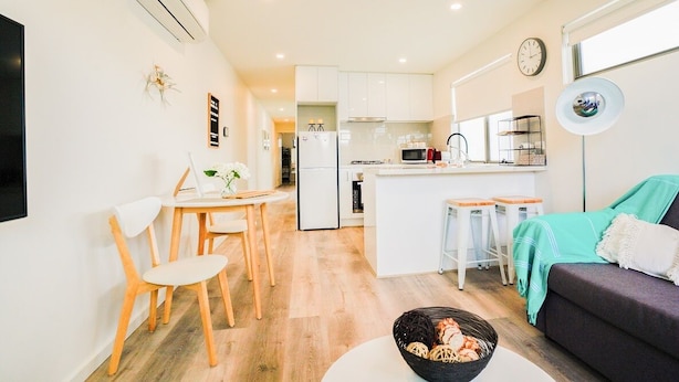 A modern kitchen with white cabinets, a central island, and a dining area with wooden chairs. - U201 Brunswick Living Top flor Balcony Close to APT n CBD FreeWifi Tram Doorstep (Brunswick West)