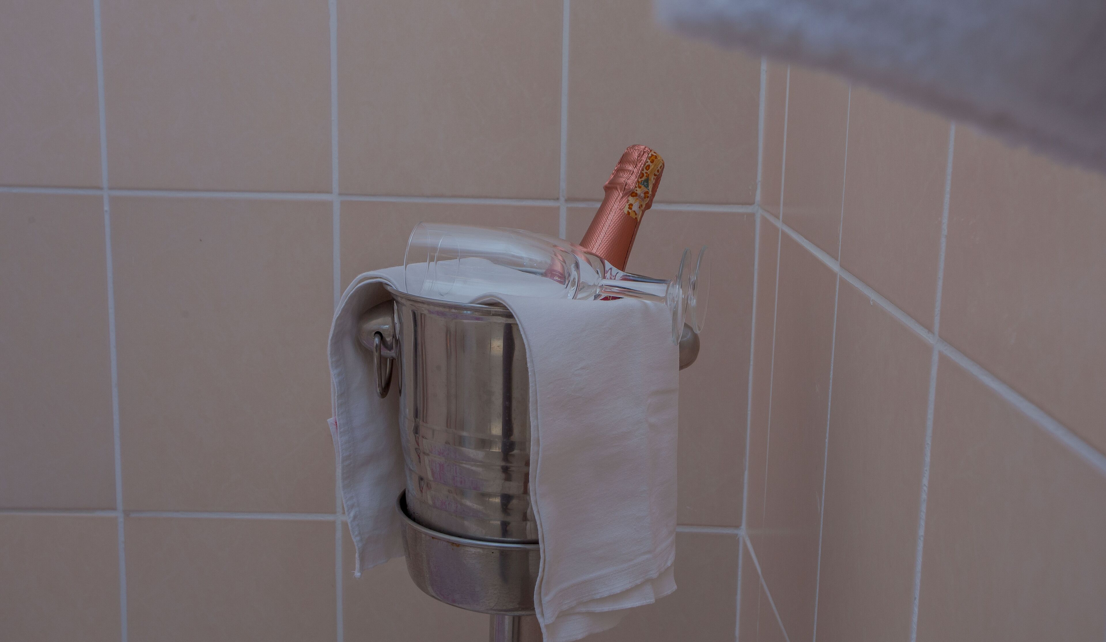 A towel dispenser with a bottle of champagne in a tiled bathroom.
