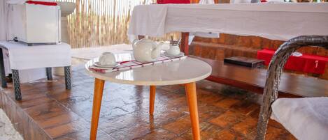 Una mesa con una tetera y tazas, un mantel blanco y una toalla roja sobre un piso de madera.